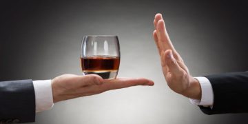 Close-up Of Businessman Hand Reject A Glass Of Whisky Offered By Businessperson